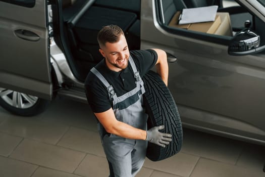 Changing tires season. Man in uniform is working in the autosalon at daytime.