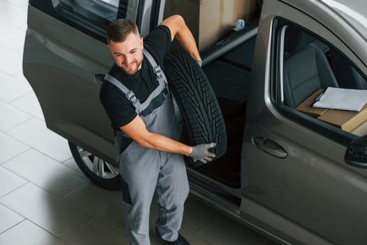Changing tires season. Man in uniform is working in the autosalon at daytime.