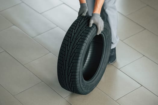 Changing tires season. Man in uniform is working in the autosalon at daytime.