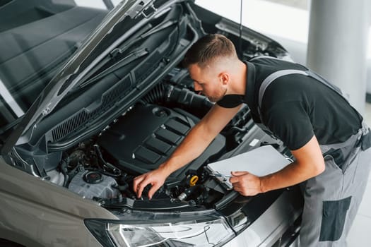 Busy man in uniform is working in the autosalon at daytime.