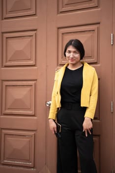 Beautiful asian woman (LGBTQ) natural makeup wear fashion yellow leather clothes with glasses posing at old town and vintage building outdoor fashion style