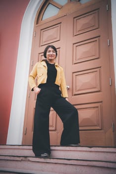 Beautiful asian woman (LGBTQ) natural makeup wear fashion yellow leather clothes with glasses posing at old town and vintage building outdoor fashion style