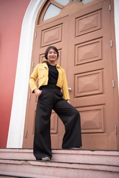 Beautiful asian woman (LGBTQ) natural makeup wear fashion yellow leather clothes with glasses posing at old town and vintage building outdoor fashion style