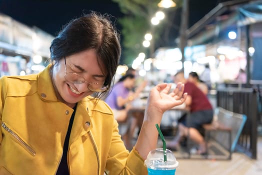 Beautiful asian woman (LGBTQ) natural makeup wear fashion yellow leather clothes with glasses posing with food or drink at thai street food, market or restaurant outdoor fashion style