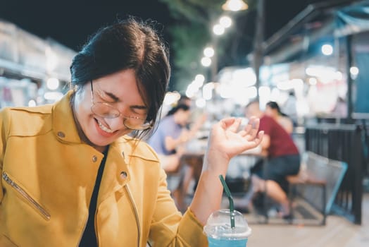 Beautiful asian woman (LGBTQ) natural makeup wear fashion yellow leather clothes with glasses posing with food or drink at thai street food, market or restaurant outdoor fashion style