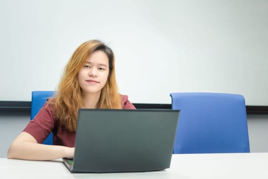 Asian woman is student, businesswoman working by computer notebook, laptop in office meeting room with whiteboard in background with happy and relax emotion in concept working woman, success in life