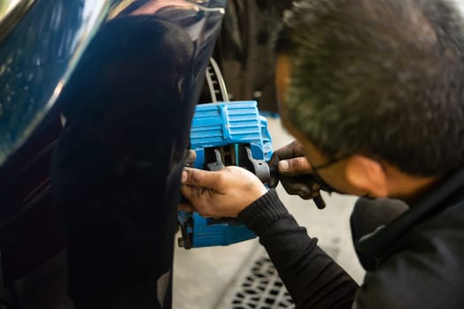 Car mechanic or serviceman disassembly and checking a disc brake and asbestos brake pads for fix and repair problem at car garage or repair shop