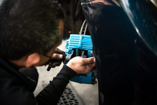 Car mechanic or serviceman disassembly and checking a disc brake and asbestos brake pads for fix and repair problem at car garage or repair shop