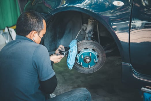 Car mechanic or serviceman disassembly and checking a disc brake and asbestos brake pads for fix and repair problem at car garage or repair shop