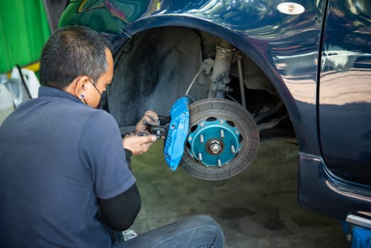 Car mechanic or serviceman disassembly and checking a disc brake and asbestos brake pads for fix and repair problem at car garage or repair shop