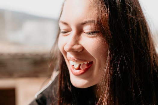 Happy young smiling woman with freckles outdoors portrait. Soft sunny colors. Outdoor close-up portrait of a young brunette woman and looking to the camera, posing against nature background.