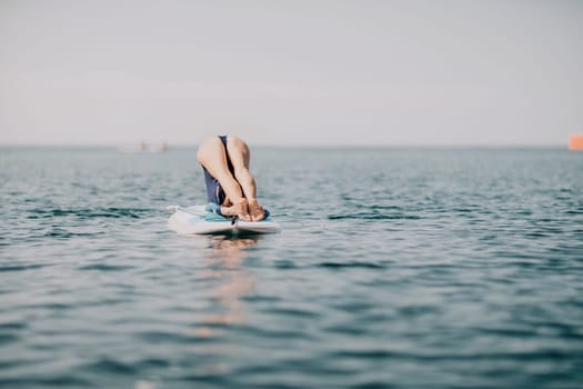 Woman sup yoga. Middle age sporty woman practising yoga pilates on paddle sup surfboard. Female stretching doing workout on sea water. Modern individual hipster outdoor summer sport activity