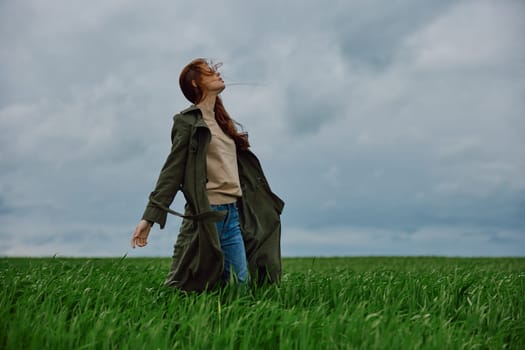 a woman in a dark coat with long red hair stands in a field against a cloudy sky in windy weather. High quality photo