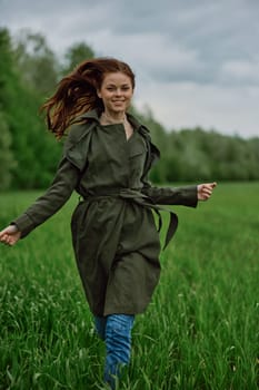 a beautiful woman in a long raincoat runs across a field in high grass in spring in cloudy weather. High quality photo