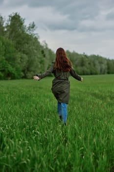 a woman in a long raincoat runs across a field in tall green grass in cloudy weather in spring. High quality photo