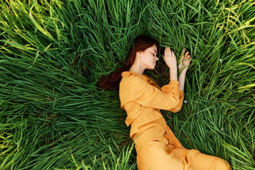 a relaxed woman enjoys summer lying in the tall green grass with her eyes closed. Photo taken from above. High quality photo