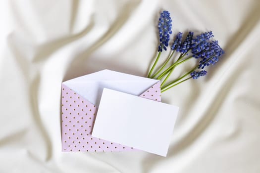 Pink envelope with blank card and muscari flower on white background. Top view