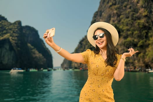 Cheerful woman in summer clothes making self with mobile phone against sea background. People vacation lifestyle journey concept.
