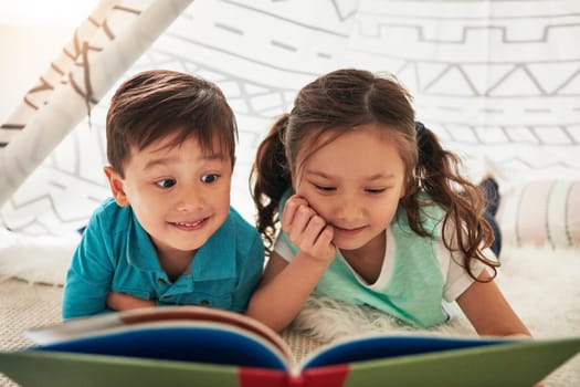 Letting their imagination and curiosity travel through books. two adorable young siblings reading a book together at home