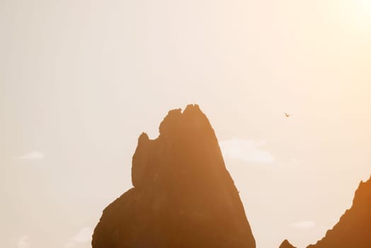 A red burning sunset with the silhouette of a cliff over the sea. Abstract nature summer or spring ocean sea background. Small waves on golden warm water surface with bokeh lights from sun.