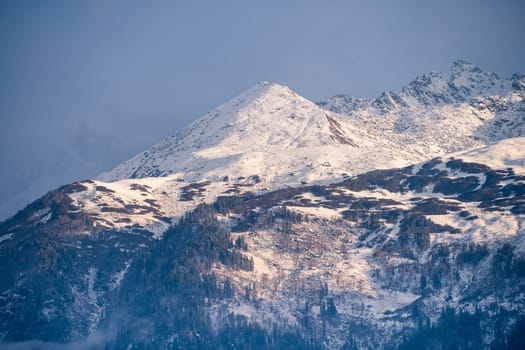 fog mist rolling over tree covered mountains in the foreground and snow capped peak in the background in manali himachal pradesh In India