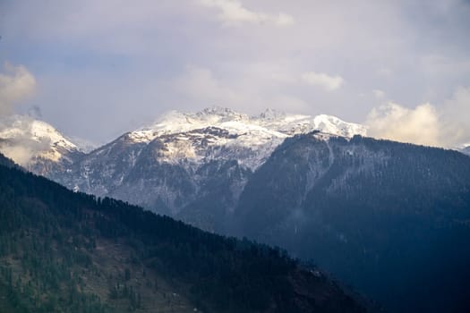 fog mist rolling over tree covered mountains in the foreground and snow capped peak in the background in manali himachal pradesh In India