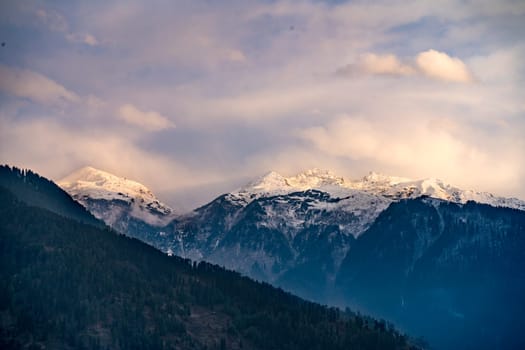 monsoon clouds moving over snow covered himalaya mountains with the blue orange sunset sunrise light over kullu manali valley India