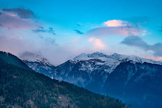 monsoon clouds moving over snow covered himalaya mountains with the blue orange sunset sunrise light over kullu manali valley India