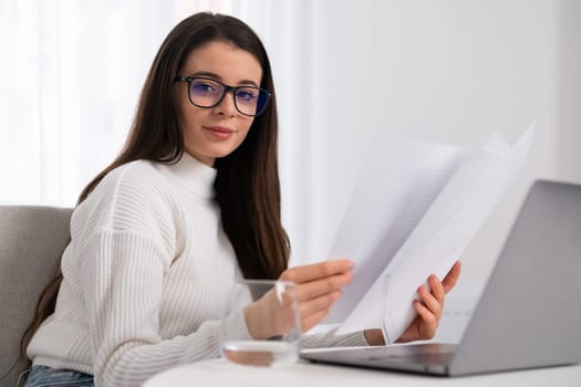 A young businesswoman in glasses works with documents and computer in the office.