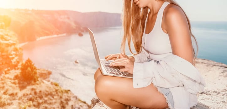 Digital nomad, Business woman working on laptop by the sea. Pretty lady typing on computer by the sea at sunset, makes a business transaction online from a distance. Freelance remote work on vacation