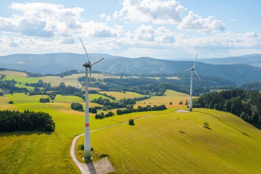 Panoramic view of windmills in the wind farm in the yellow field and mountains on the background. Production of green and renewable energy.