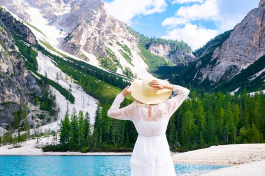 Beautiful woman in a white dress walking on the shore of Lake Braies with an amazing view of the alps.