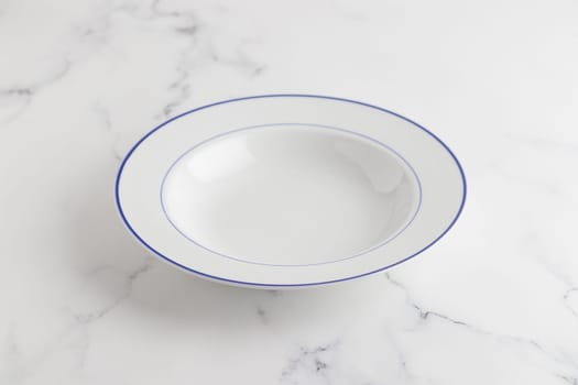Empty white soup plate with blue stripe on a white background