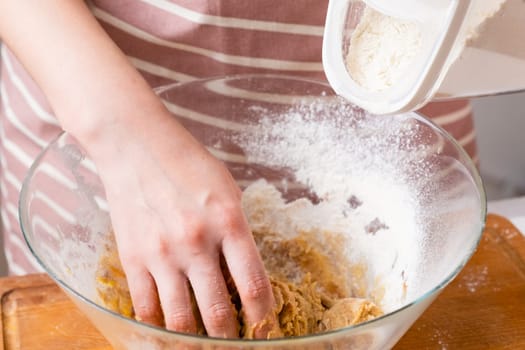 Close up of woman baker hands kneading the dough and add flour in the mixing bowl. Homemade pastry for cakes or cookies.