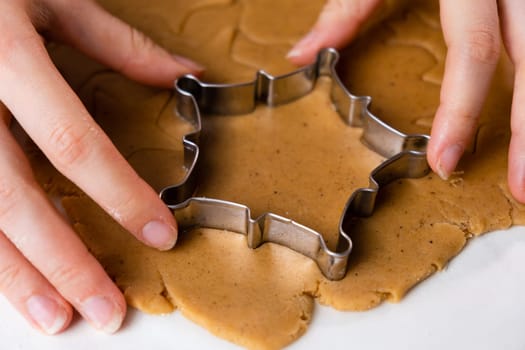 Close up woman hands cutting out cookies with metal mold from the shortcrust pastry. A metal forms in the form of snowflakes for making gingerbread for Christmas.