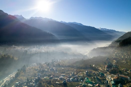 aerial drone shot gaining height over fog covered valley town of manali hill station with himalaya range in distance showing this popular tourist destination in India