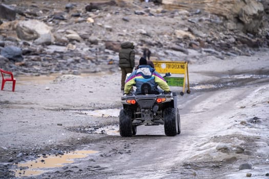 Manali, India - circa 2023: crowd of people at lahul spiti showing small food outlets, adventure sports with family riding ATV on the snow covered road with himalay peaks in the distance