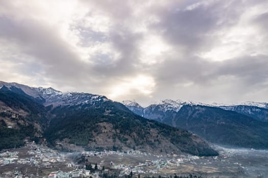 monsoon clouds moving over snow covered himalaya mountains with the blue orange sunset sunrise light with town of kullu manali valley at the base of mountains India