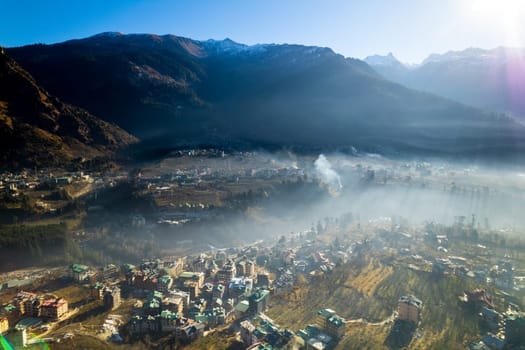 aerial drone shot gaining height over fog covered valley town of manali hill station with himalaya range in distance showing this popular tourist destination in India