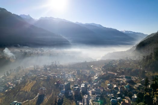 aerial drone shot gaining height over fog covered valley town of manali hill station with himalaya range in distance showing this popular tourist destination in India