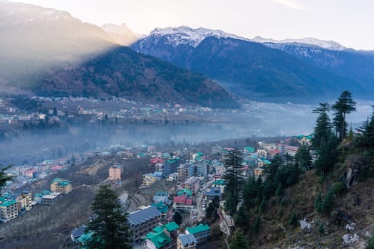 monsoon clouds moving over snow covered himalaya mountains with the blue orange sunset sunrise light with town of kullu manali valley at the base of mountains India