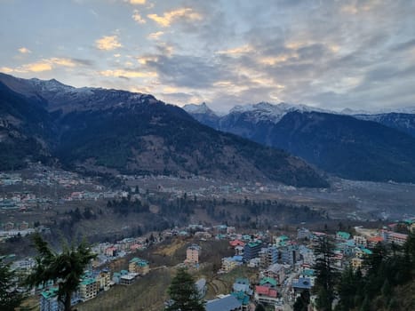 monsoon clouds moving over snow covered himalaya mountains with the blue orange sunset sunrise light with town of kullu manali valley at the base of mountains India