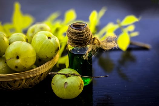 Close-up of Indian gooseberry with its extracted essence or concentration in a transparent bottle on a wooden surface with raw amla in a fruit and vegetable basket.