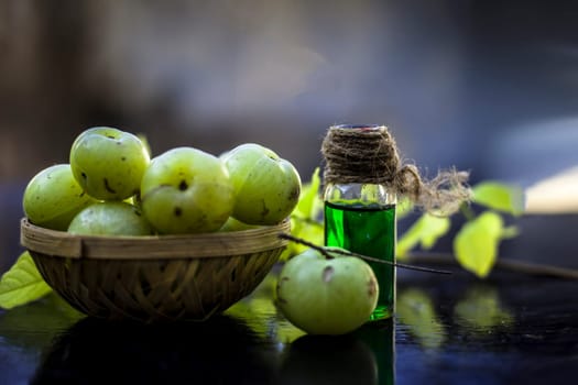 Close-up of Indian gooseberry with its extracted essence or concentration in a transparent bottle on a wooden surface with raw amla in a fruit and vegetable basket.