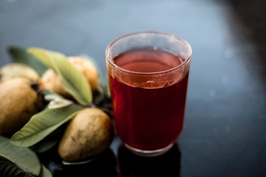 Close-up of organic juice of red guava or amarood or jamrukh in a transparent glass with raw guava and its leaves on the wooden surface.