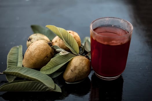 Close-up of organic juice of red guava or amarood or jamrukh in a transparent glass with raw guava and its leaves on the wooden surface.