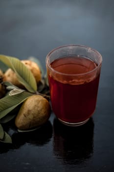 Close-up of organic juice of red guava or amarood or jamrukh in a transparent glass with raw guava and its leaves on the wooden surface.