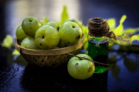 Close-up of Indian gooseberry with its extracted essence or concentration in a transparent bottle on a wooden surface with raw amla in a fruit and vegetable basket.