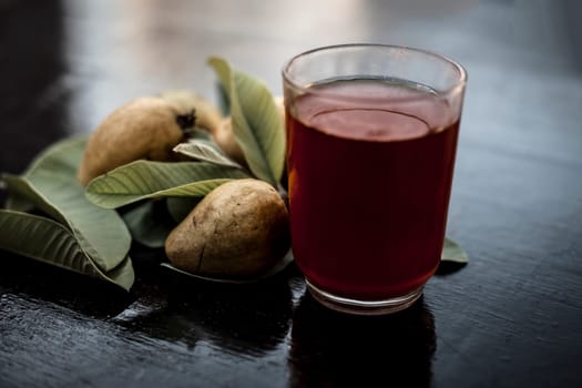 Close-up of organic juice of red guava or amarood or jamrukh in a transparent glass with raw guava and its leaves on the wooden surface.