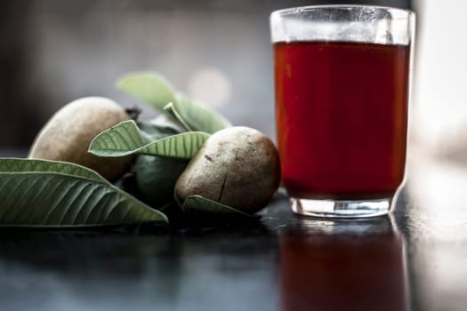 Close-up of organic juice of red guava or amarood or jamrukh in a transparent glass with raw guava and its leaves on the wooden surface.